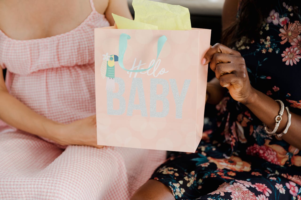 about-us-img Close-up of a pregnant woman sitting with a baby shower gift bag, celebrating motherhood.